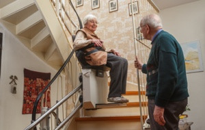 Ältere Dame fährt Treppenlift auf kurviger Treppe probe